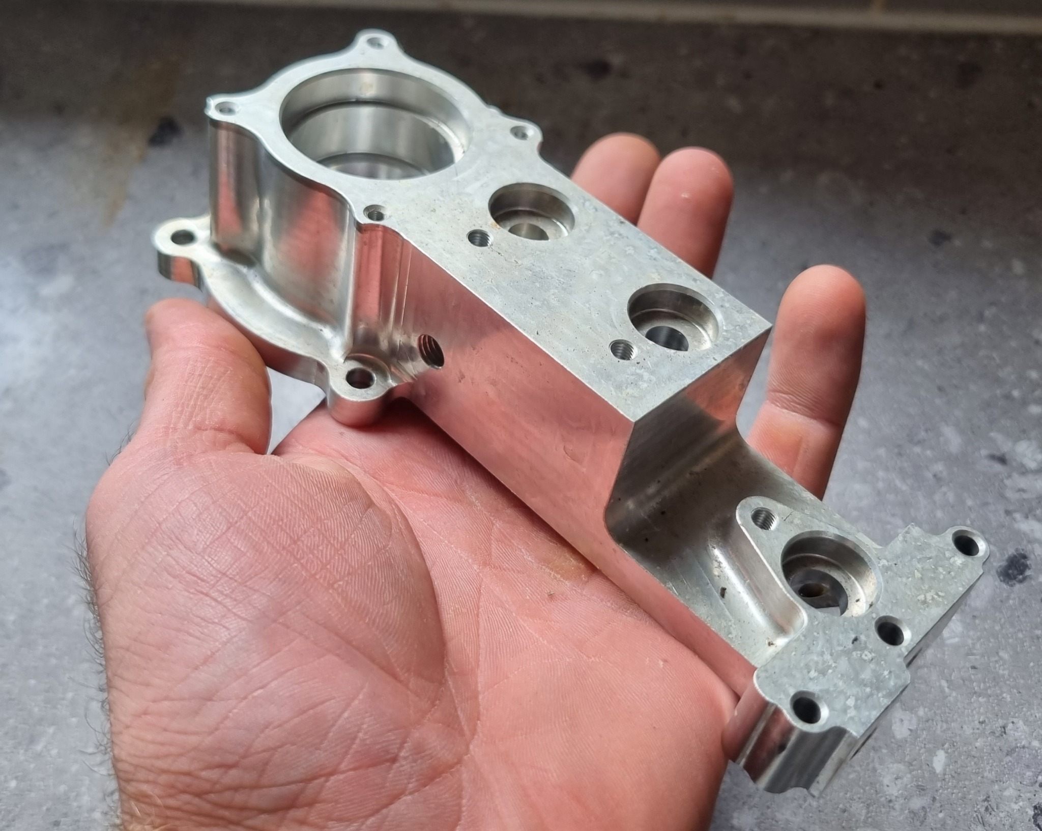 Long machined aluminium component with multiple bores and mounting features shown in hand